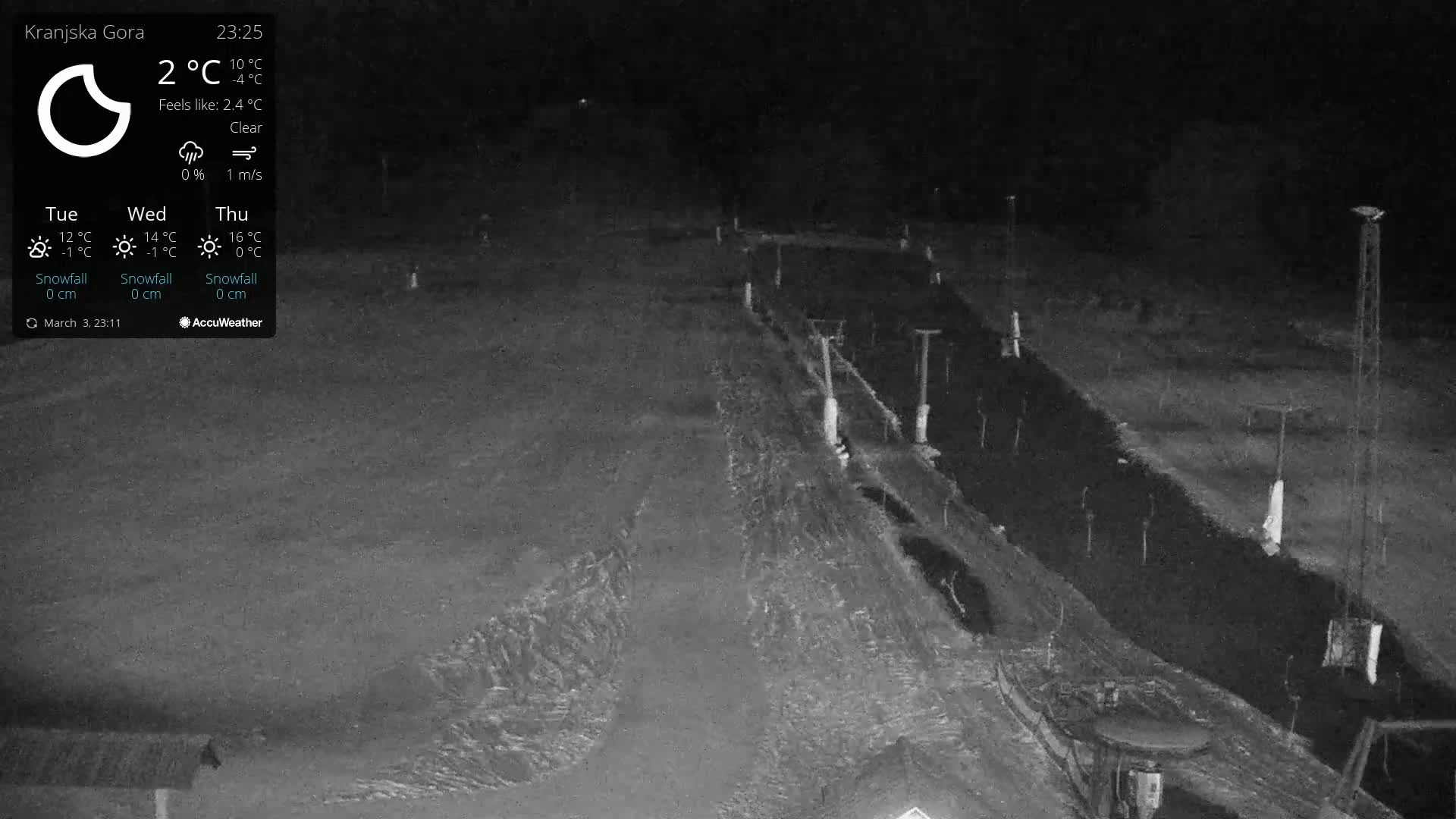 A nighttime, clear view of a snow-covered slope with several tall poles and a small structure at the bottom, under a clear sky.