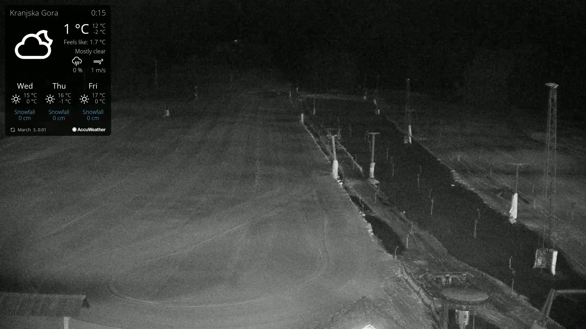 A nighttime, mostly clear view of a snow-covered area with several tall poles and a dark, possibly paved, path or road.