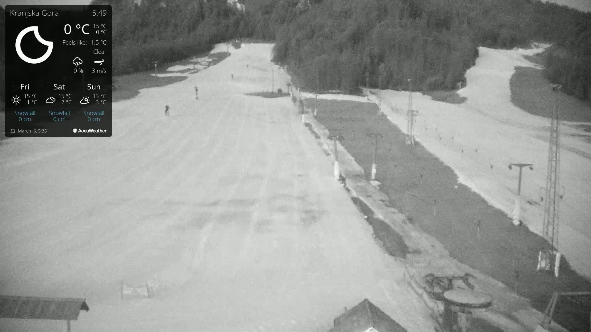 A mostly clear, nighttime view of a snow-covered ski slope with several lift poles and a few people visible.