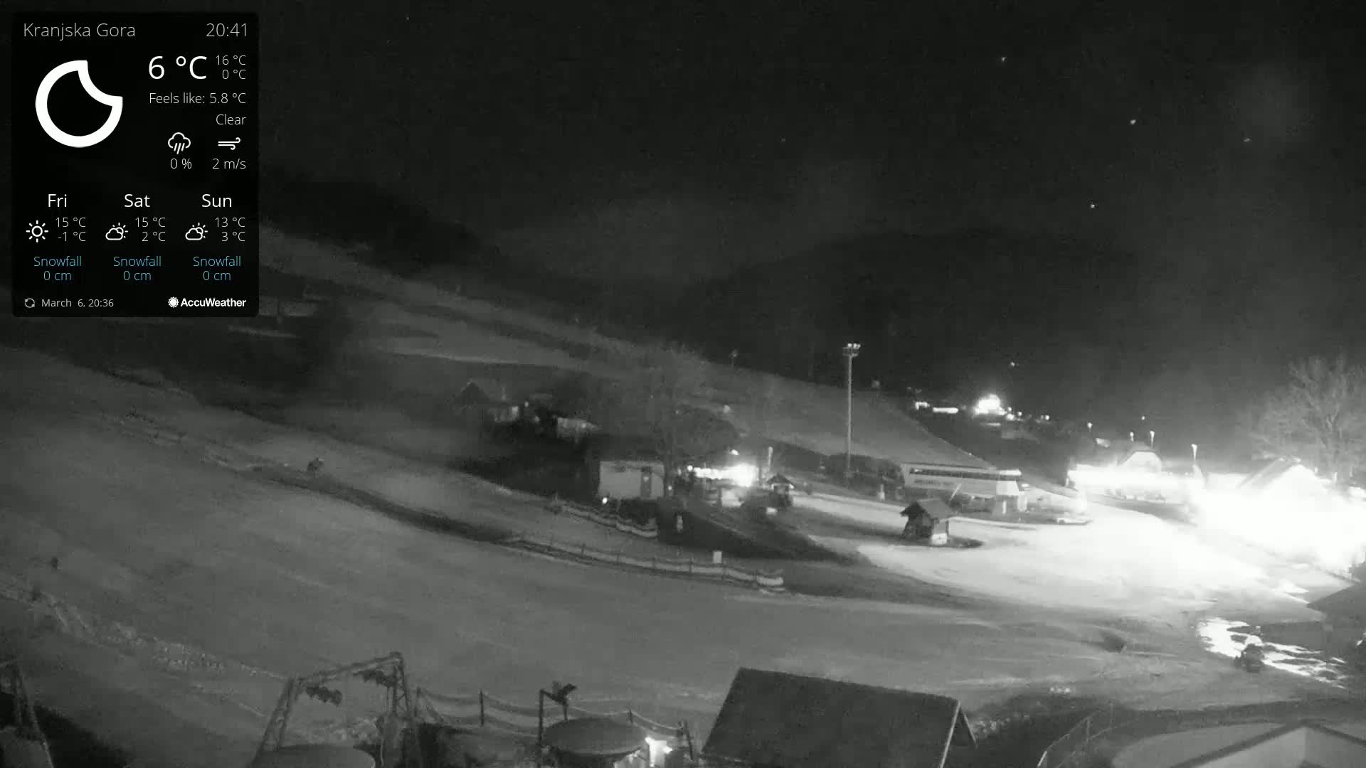 A nighttime, clear-weather view of a snow-covered ski resort with dimly lit buildings and vehicles.