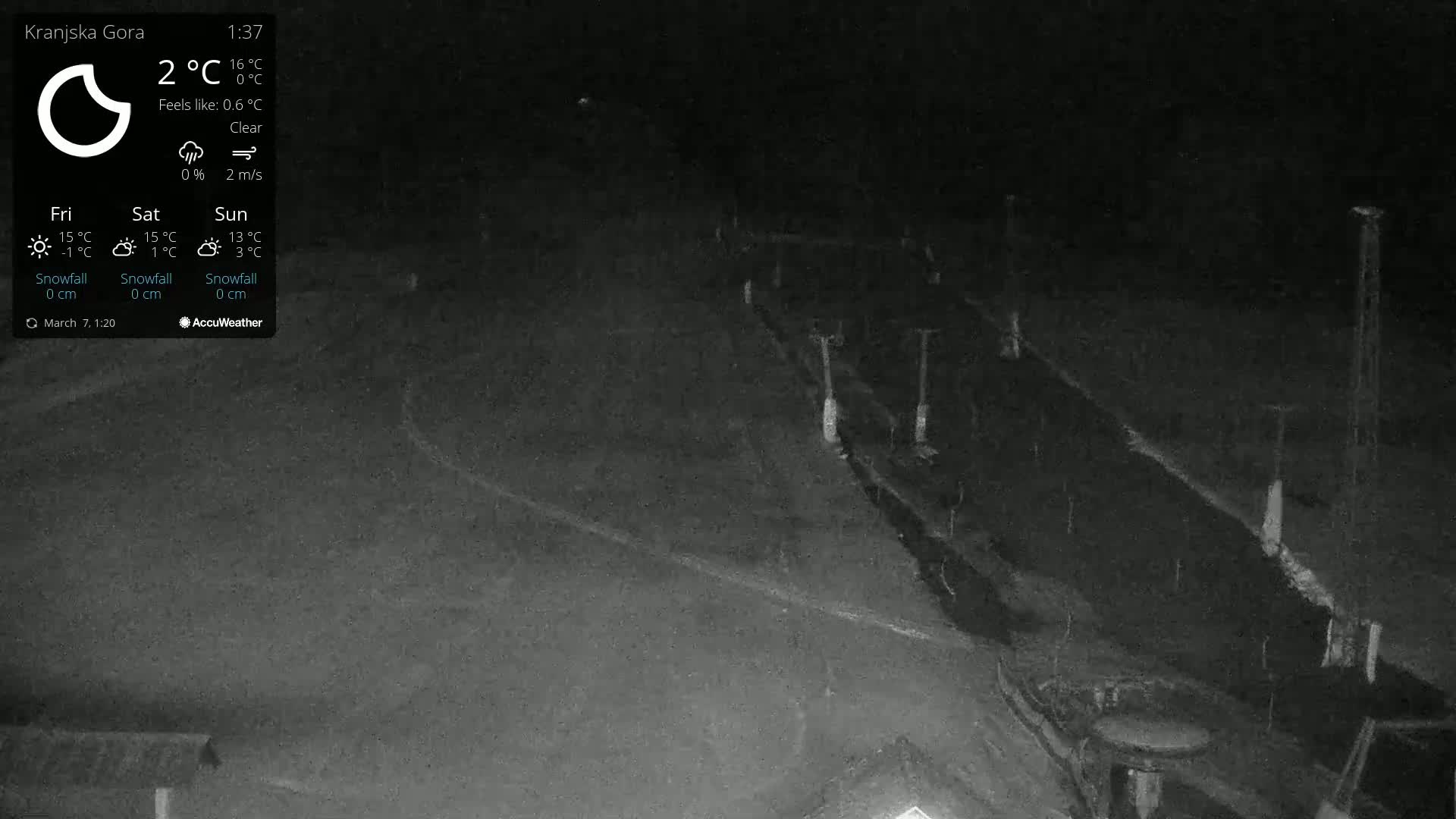 A nighttime, clear, outdoor scene shows a dark, snow-covered area with some faint structures and lights.
