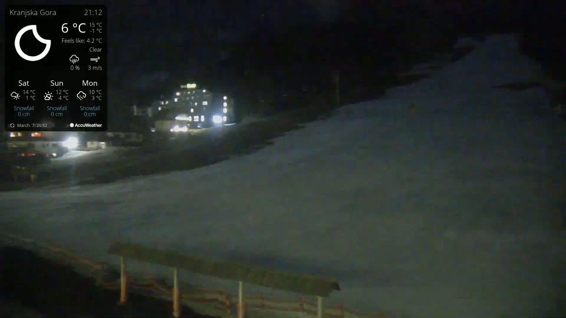 A nighttime, clear view of a snow-covered slope with a building in the background under a clear sky.