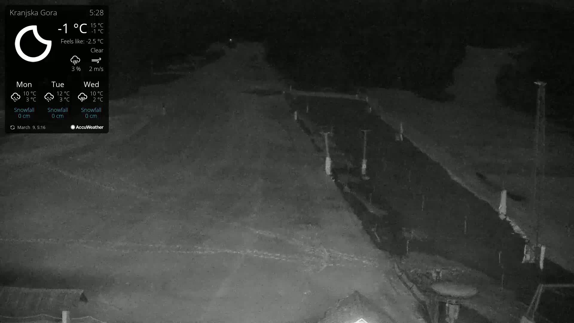 A nighttime, clear-weather view of a snow-covered, sloped area with some lights and structures visible in the distance.