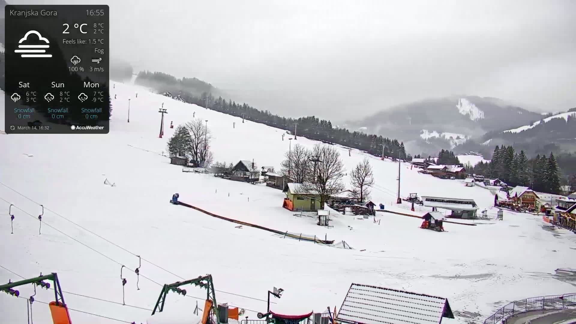 A snowy ski resort is visible on a foggy day, with several buildings and ski lifts scattered across the snow-covered slopes.