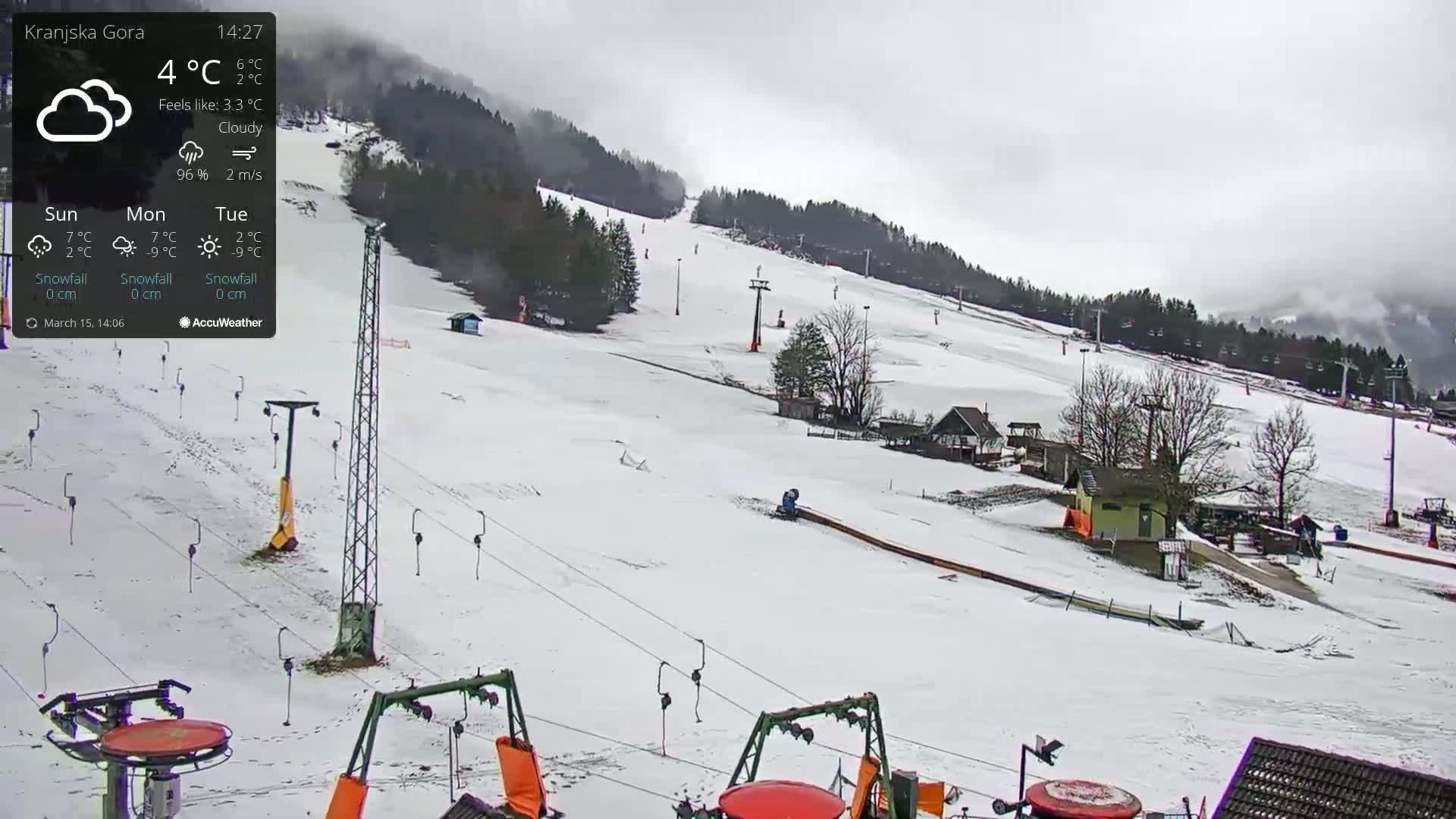 A snow-covered ski slope with chairlifts and a few small buildings under a cloudy sky.