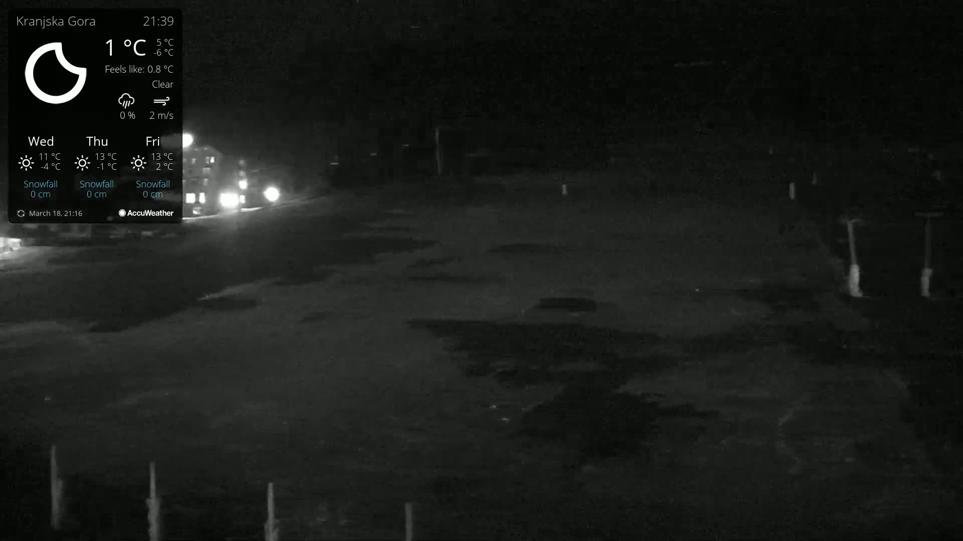 A nighttime, clear, outdoor scene shows a dark, mostly empty area with a few indistinct objects and distant headlights visible under a clear sky.