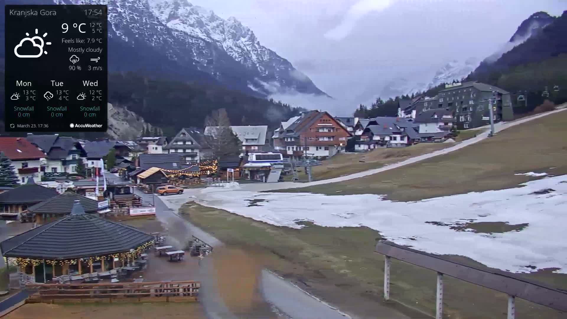 A mostly cloudy view of a snow-dusted mountain village with a ski lift, under a 9°C temperature.