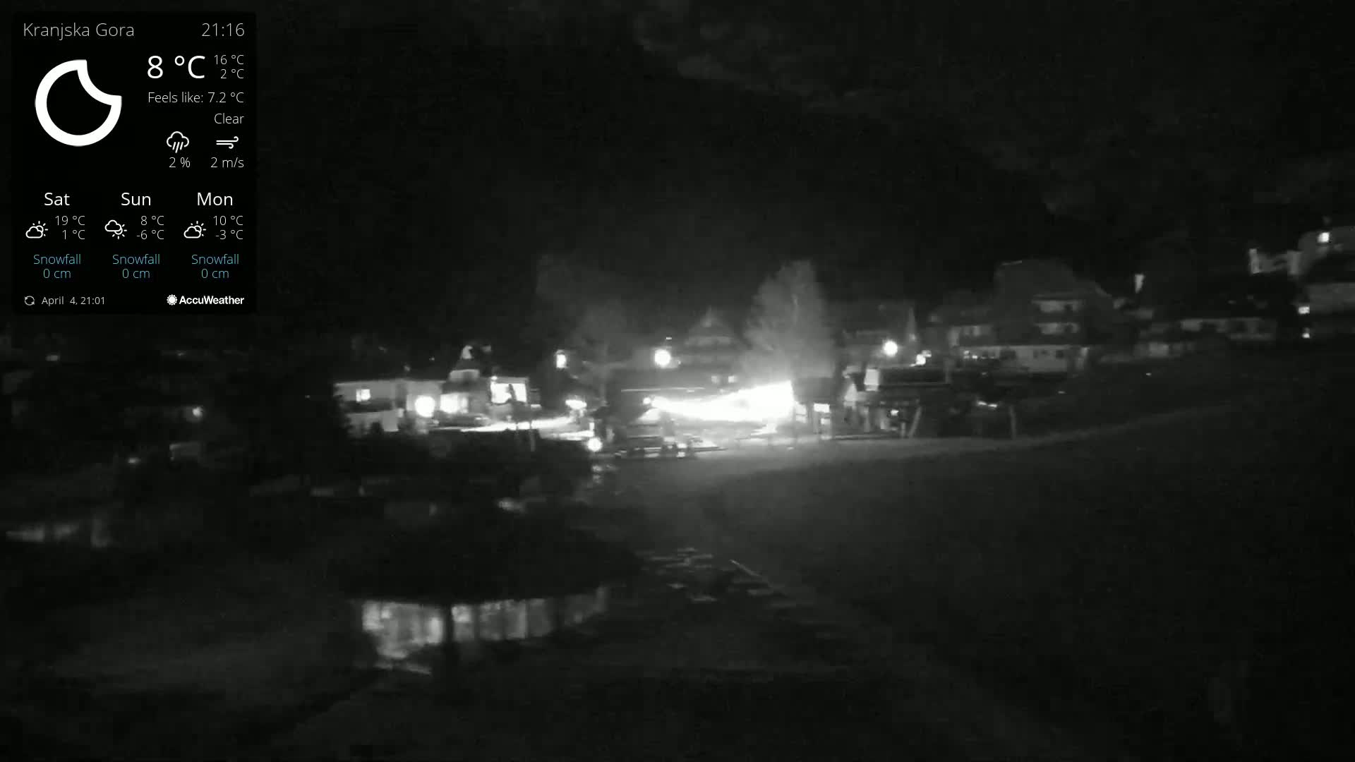 A nighttime, clear view of a small town with dimly lit buildings and a few lights visible in the distance.