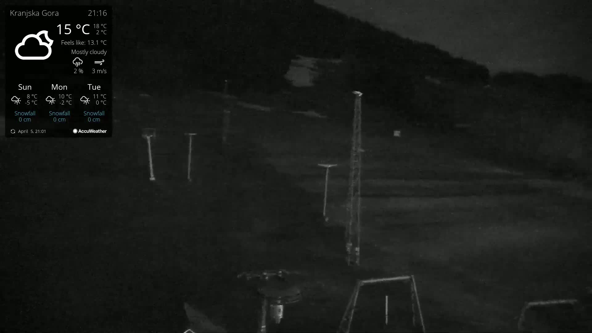 A mostly cloudy nighttime scene shows a dark, empty area with several tall, thin poles and a hill in the background.