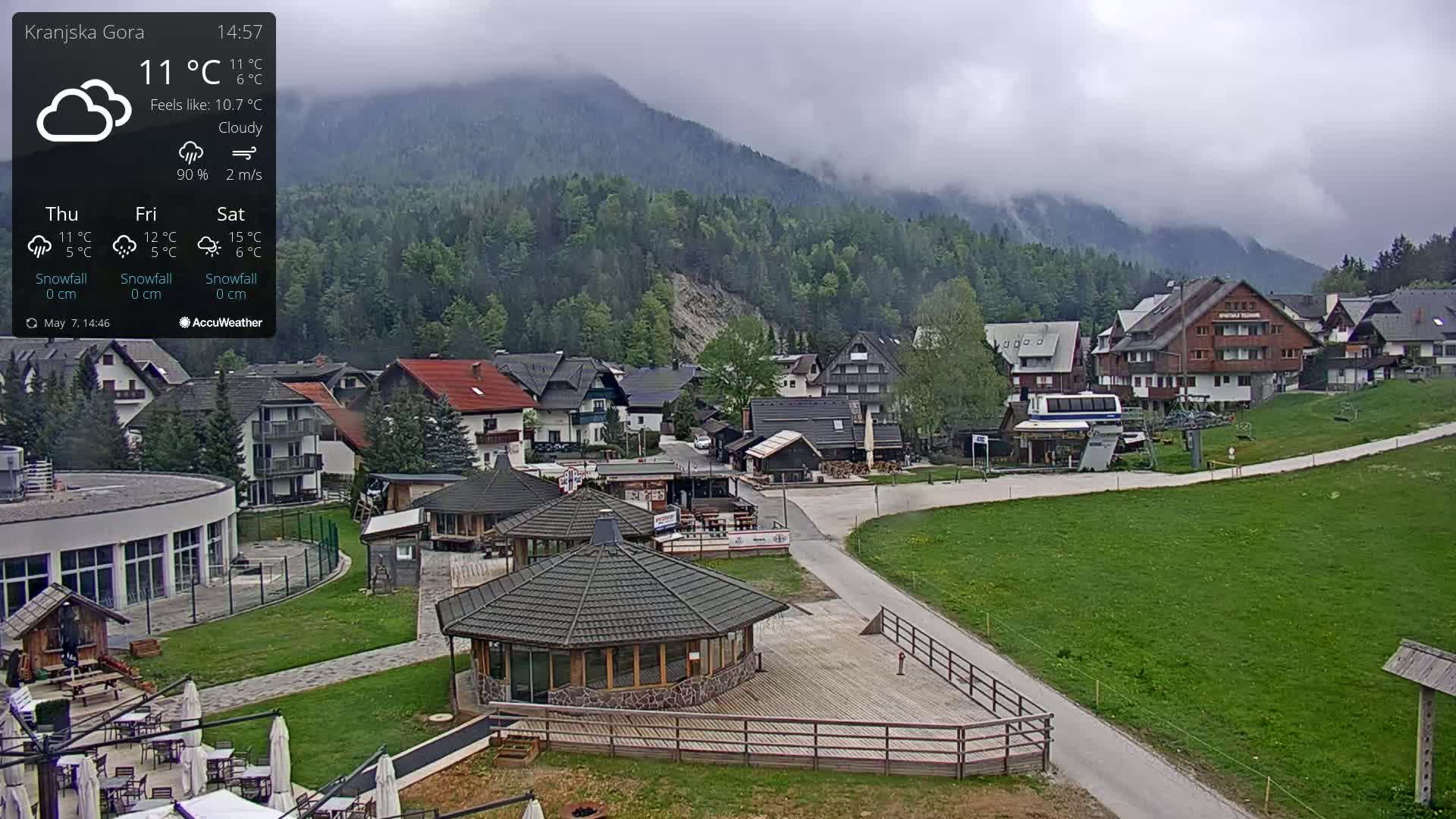 A cloudy mountain village with several buildings, a paved road, and grassy areas is shown.