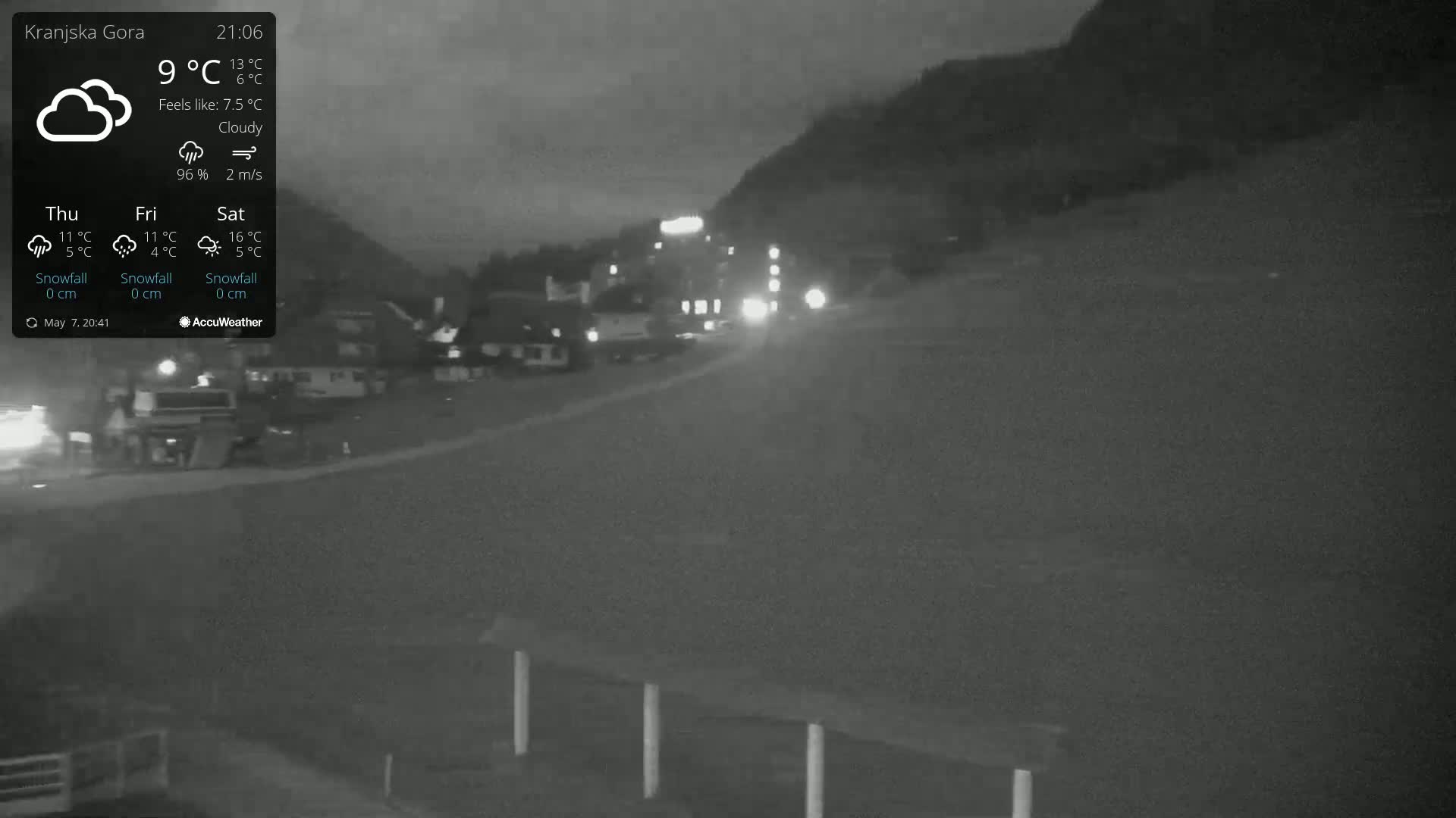 Under a cloudy night sky, several vehicles are driving on a road near a mountainside.