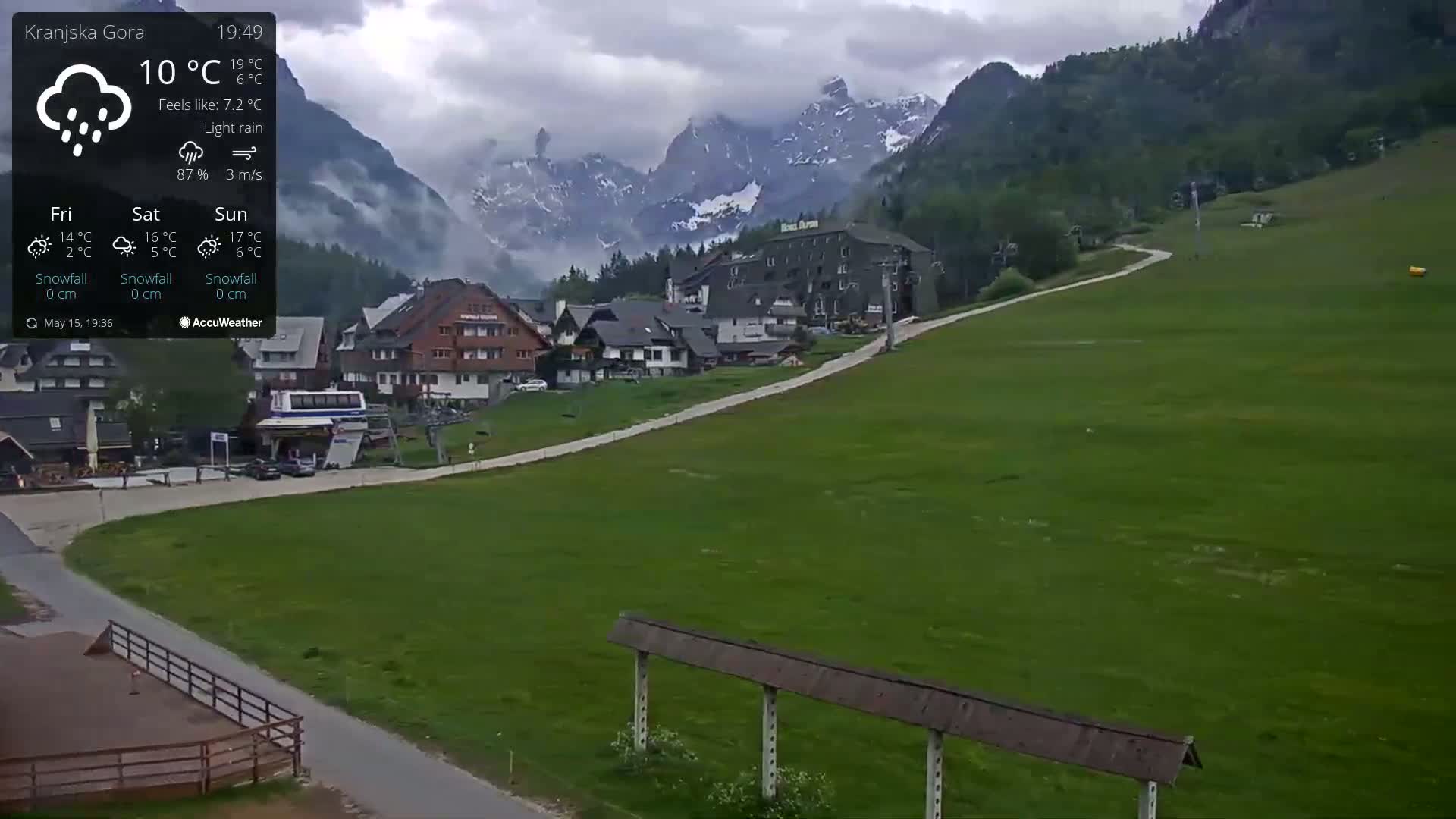 A village nestled in a valley between mountains experiences light rain under cloudy skies.