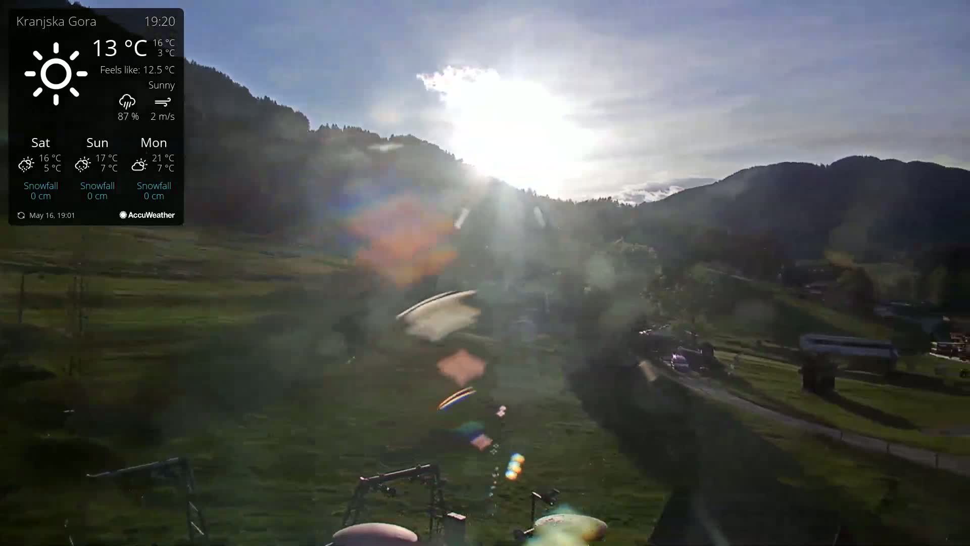 A sunny, slightly hazy view of a grassy valley nestled between mountains at sunset.