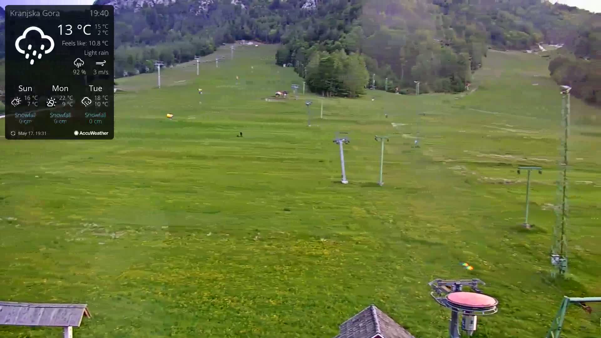 A grassy hillside with a ski lift and a few people visible under light rain.
