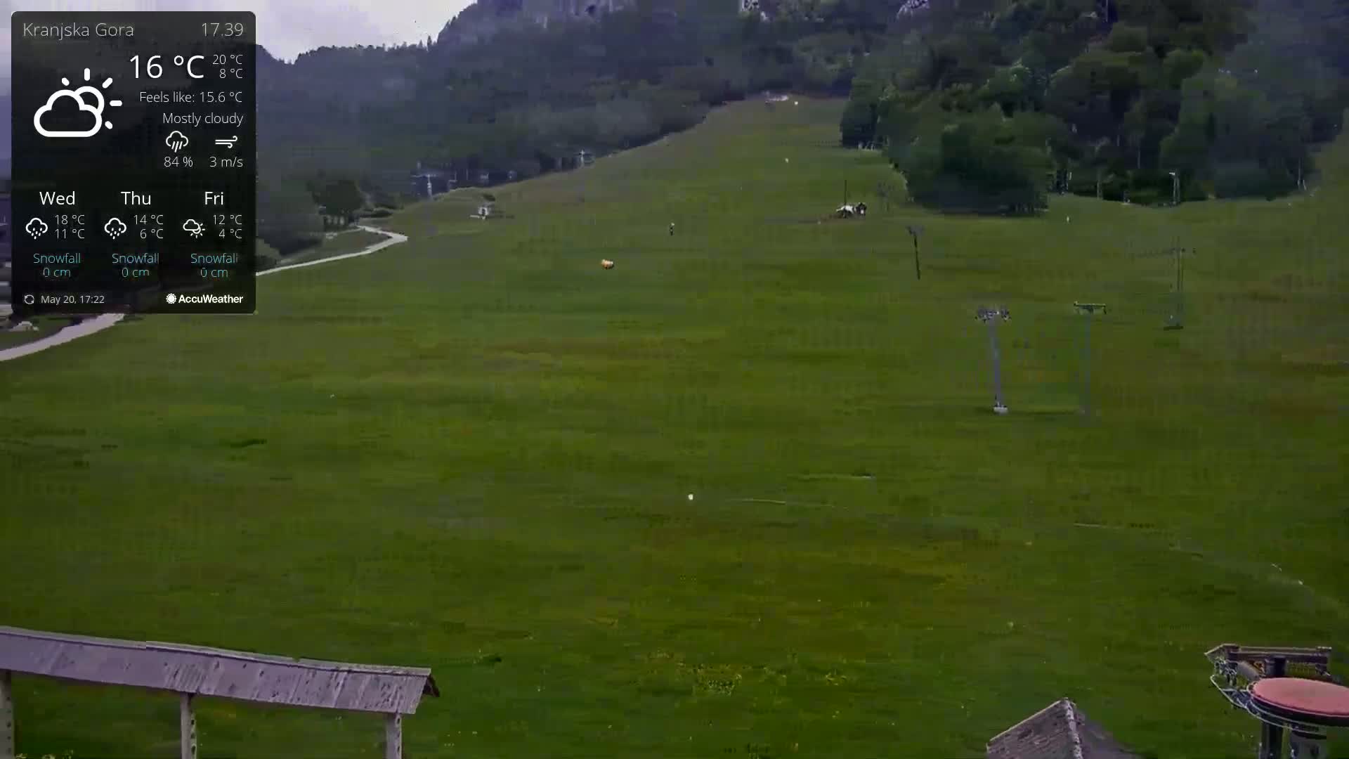 A mostly cloudy, 16°C day is shown in a long shot of a green grassy field with a ski lift and hill in the background.