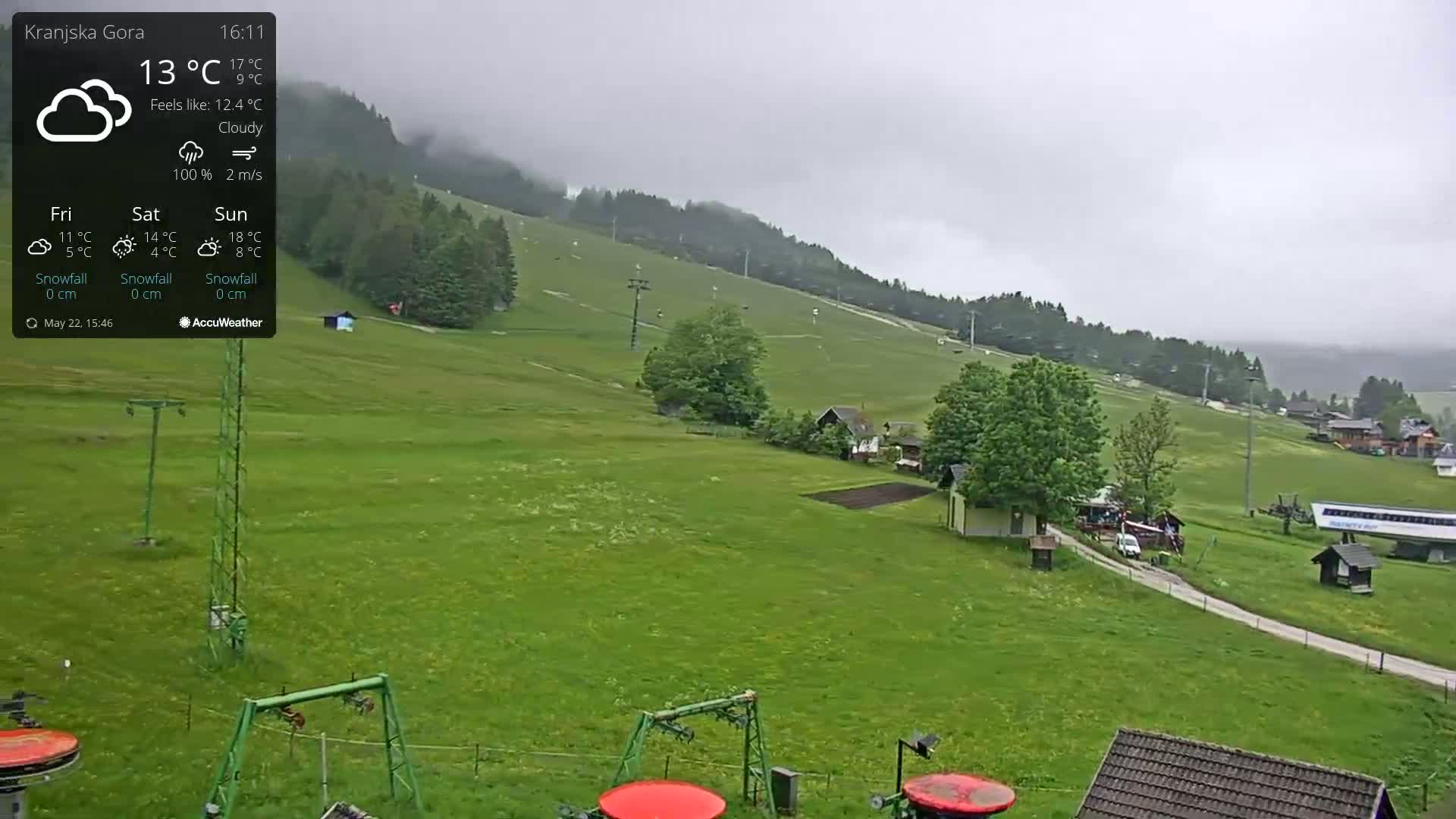 A mostly cloudy view of a grassy hillside with ski lifts, a few buildings, and a road under overcast skies.