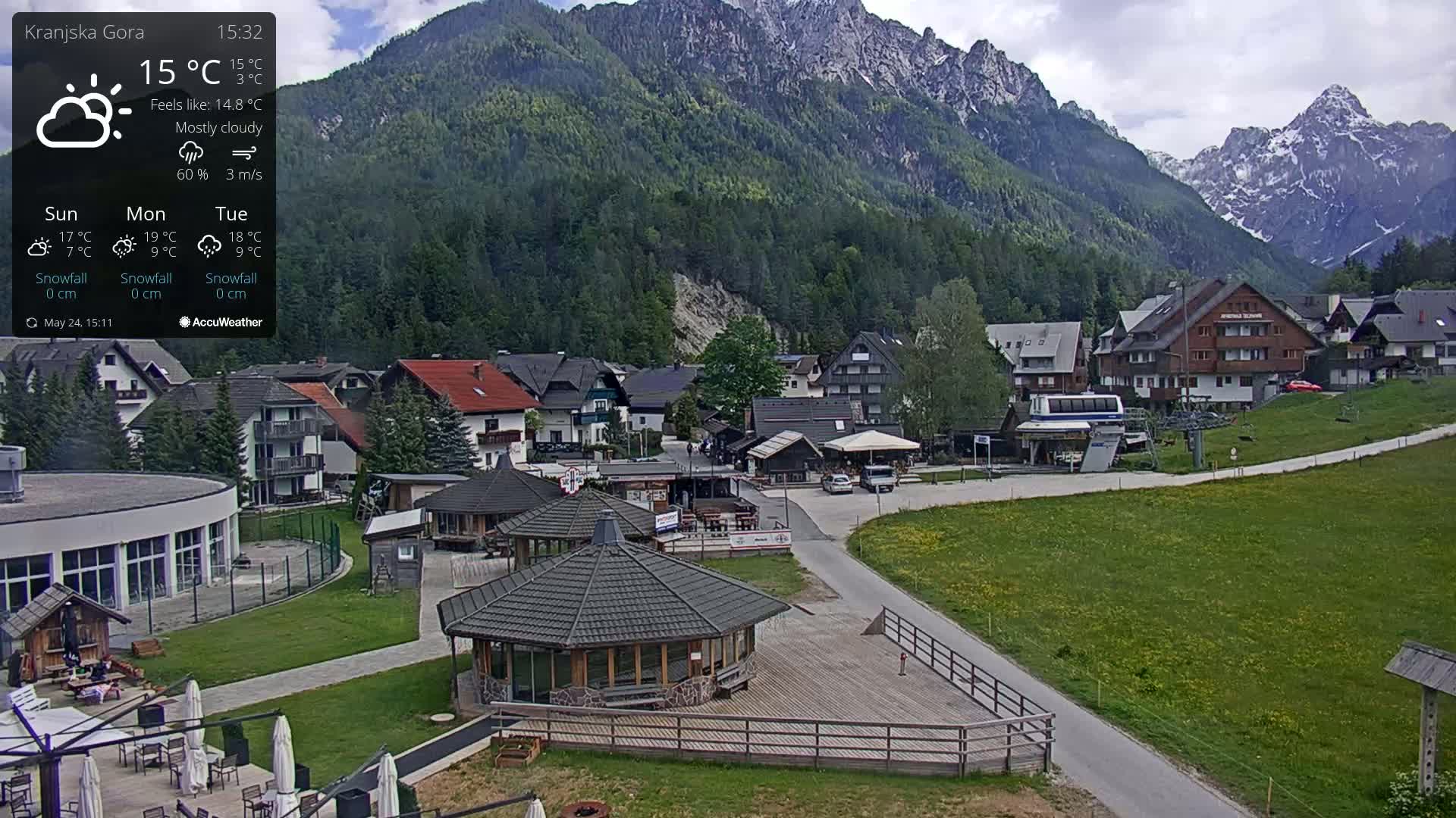 A mostly cloudy, mountain village with a cable car and several buildings, including a gazebo, is visible under a mostly cloudy sky.