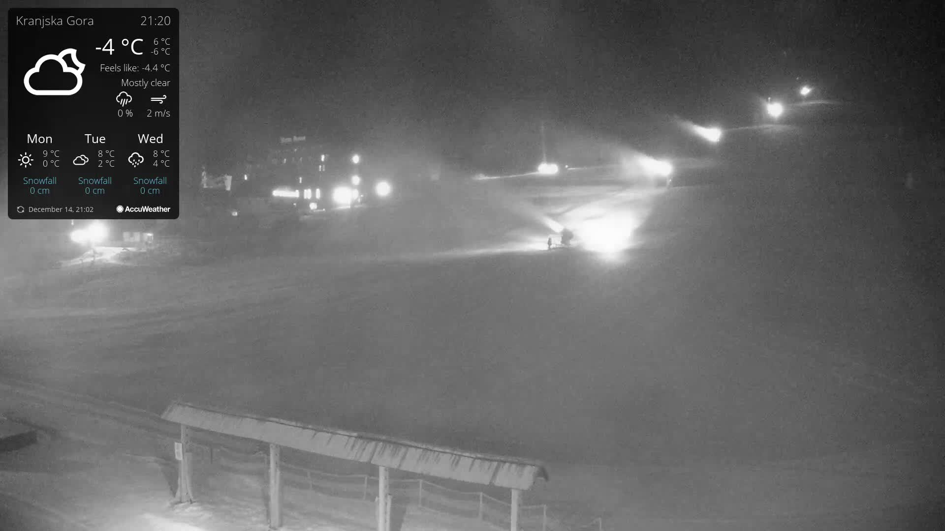 On a cold day with light snow, a snow-covered ski slope is visible, featuring numerous ski lifts, a bordering winter forest, and a few people along with a snow cannon.