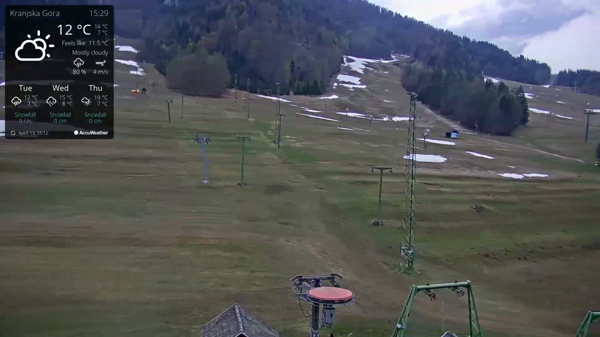 On a cold day with light snow, a snow-covered ski slope is visible, featuring numerous ski lifts, a bordering winter forest, and a few people along with a snow cannon.