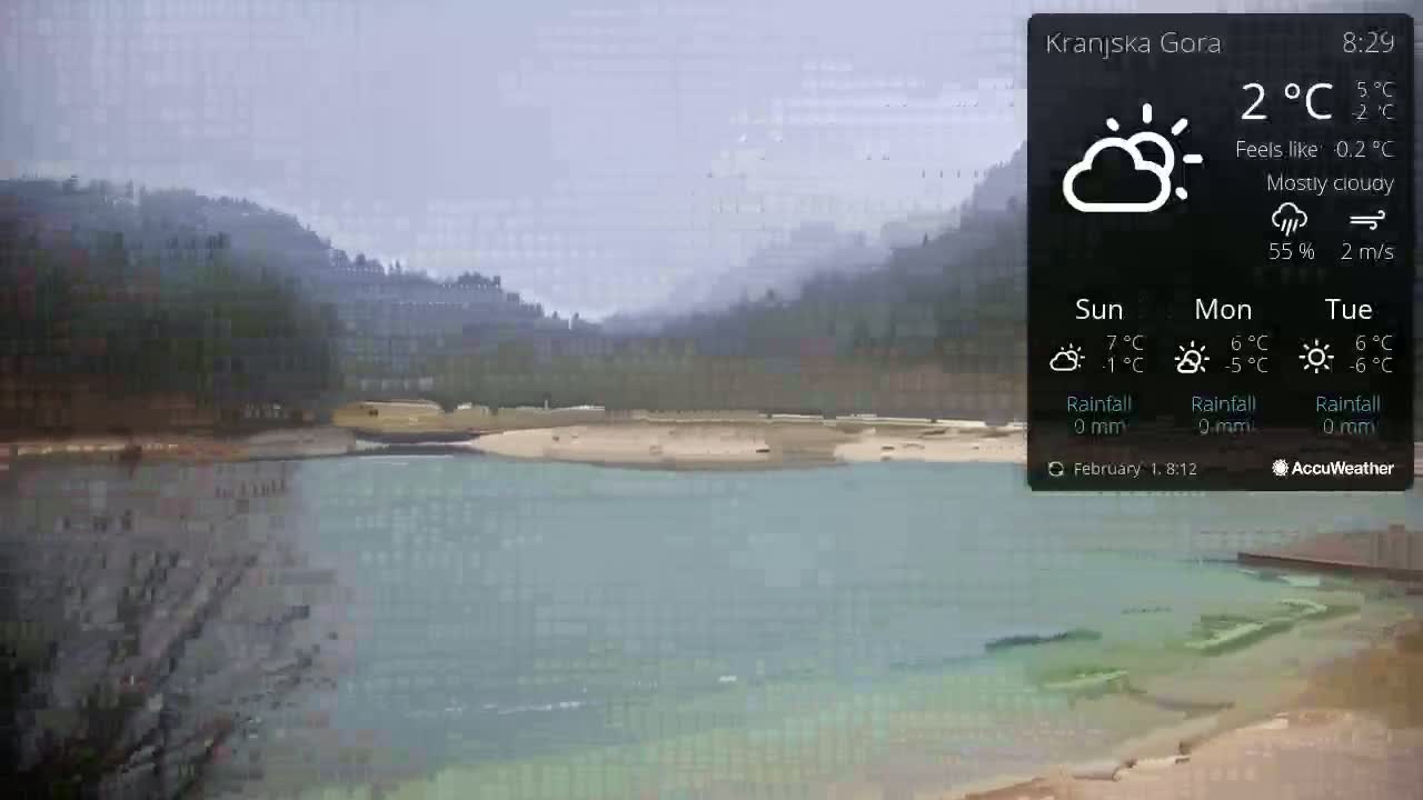 A mostly cloudy, calm day reveals a tranquil lake nestled beside tree-covered hills.