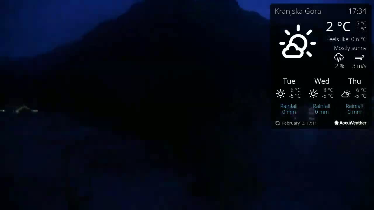 A mostly sunny, dark-blue twilight scene shows a dark mountain range with a few lights visible in the lower left corner.