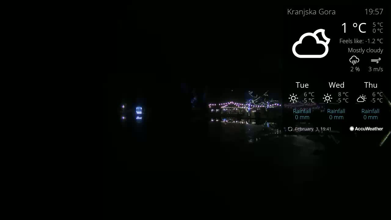 A nighttime scene of a body of water reflecting lights from a structure adorned with string lights under mostly cloudy skies.