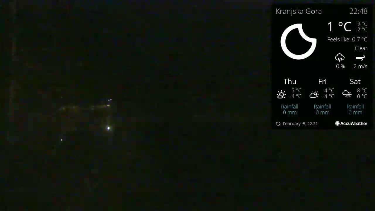 A nighttime, clear view of dimly lit structures and faint lights in the distance under a 1°C temperature.