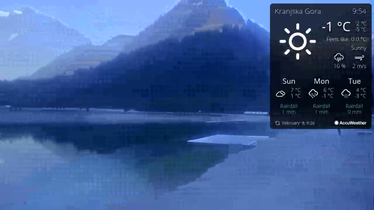 A calm, sunny lake reflects dark mountains under a clear, cold sky.