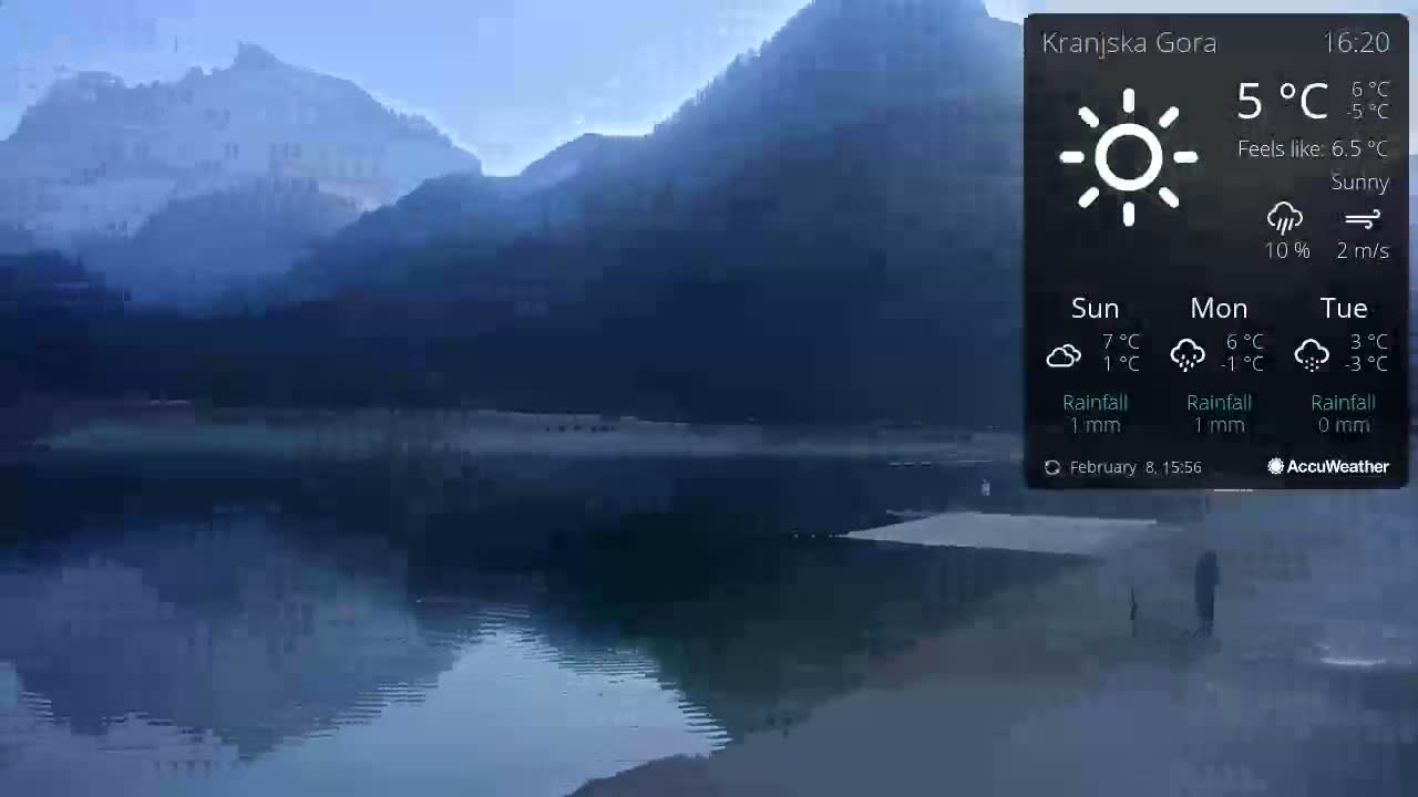 A calm lake reflects hazy mountains under a sunny sky.