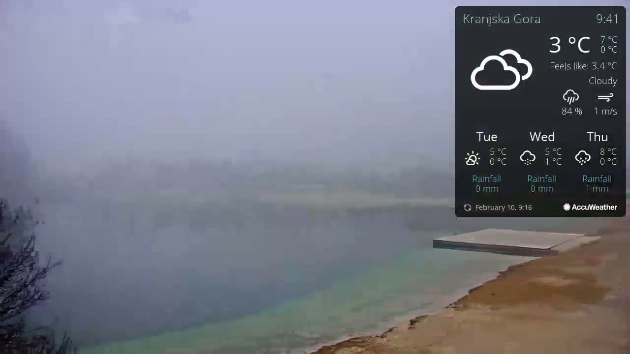 A foggy, cloudy view of a calm body of water with a flat platform extending into it from a sandy shore.