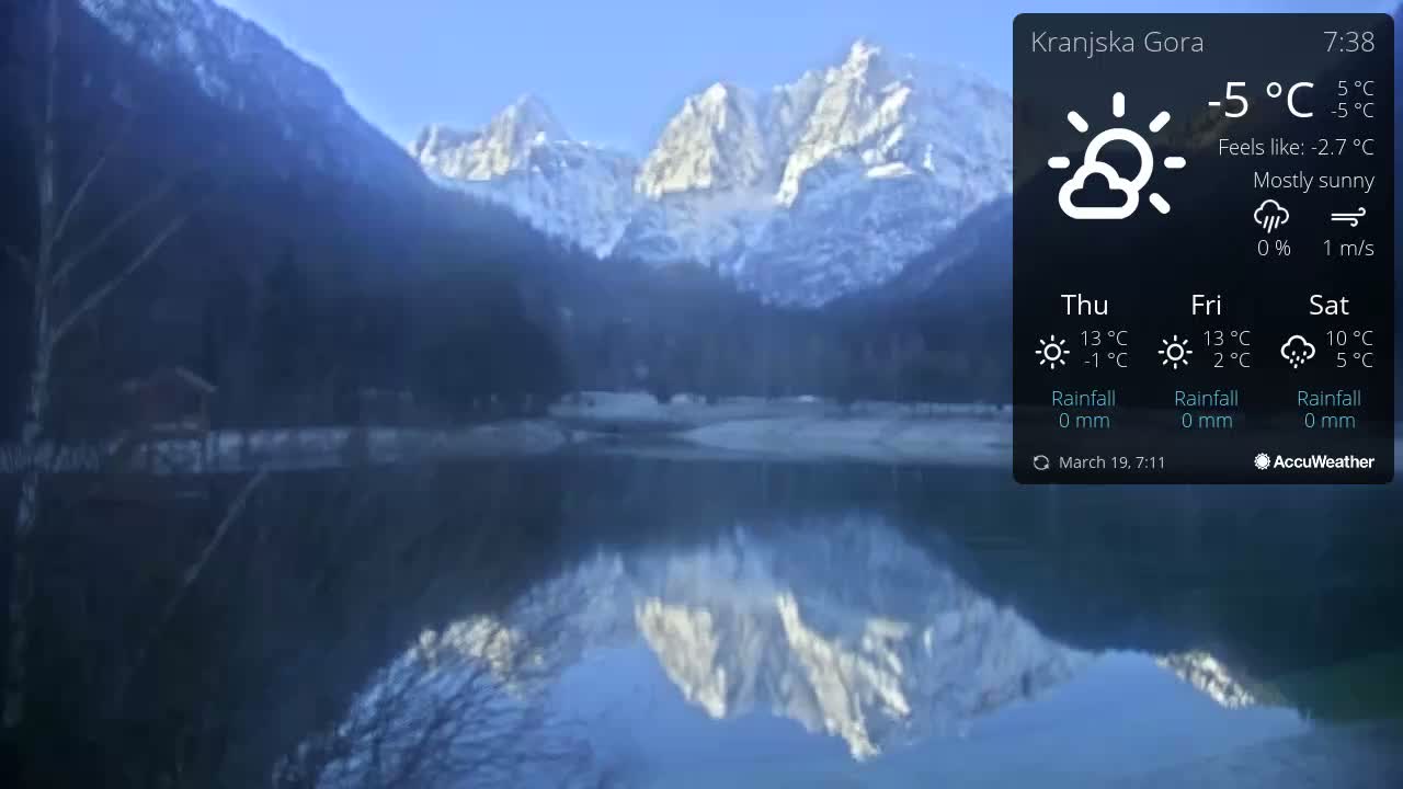 A mostly sunny, cold day shows the reflection of snow-capped mountains in a calm lake.