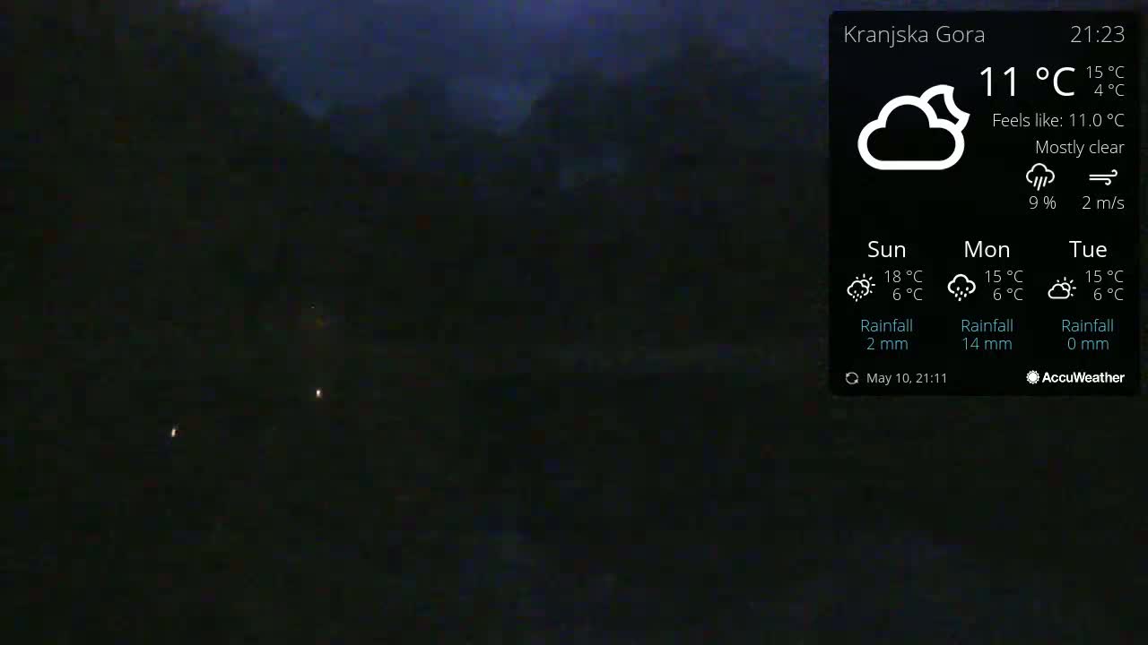 A nighttime, mostly clear outdoor scene shows a dark landscape with a few faint lights in the distance under a mostly clear sky; the temperature is 11°C.