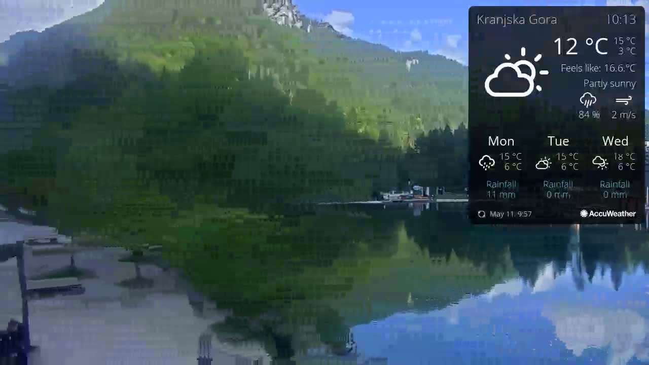 A calm lake reflects a partly sunny sky and lush green mountains under a partly sunny sky.
