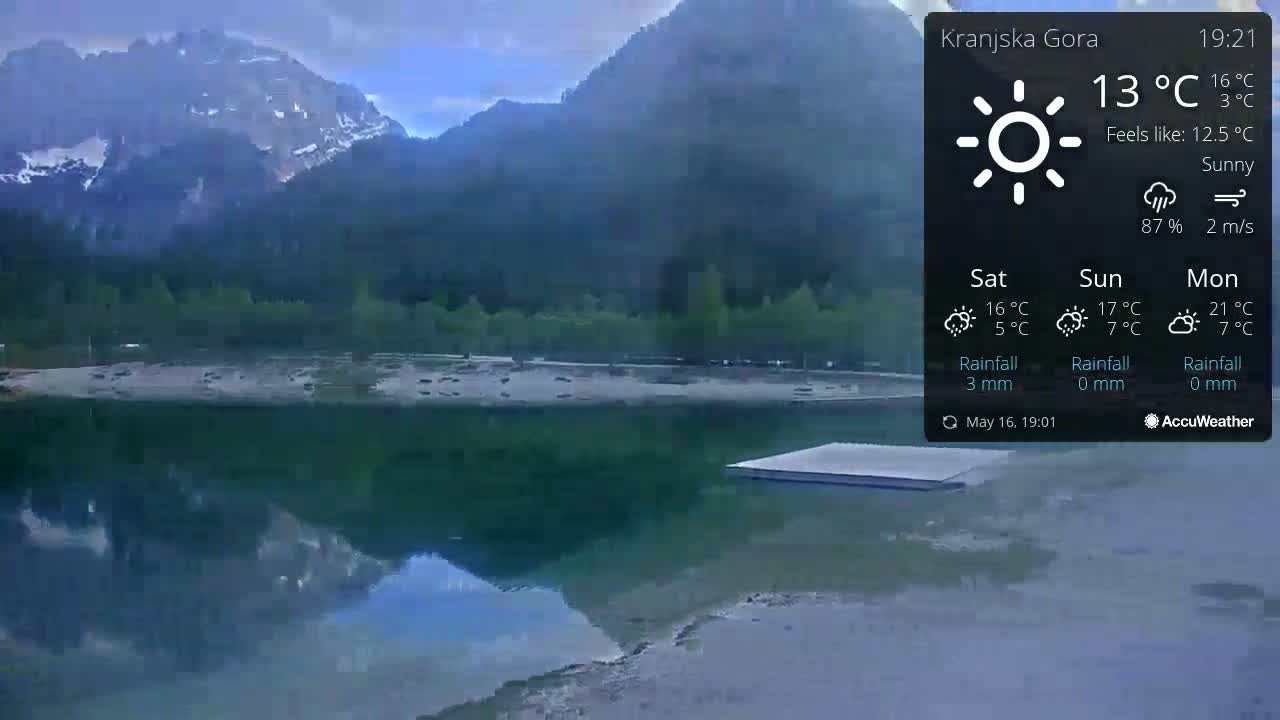 A calm lake reflects mountains under a sunny sky.