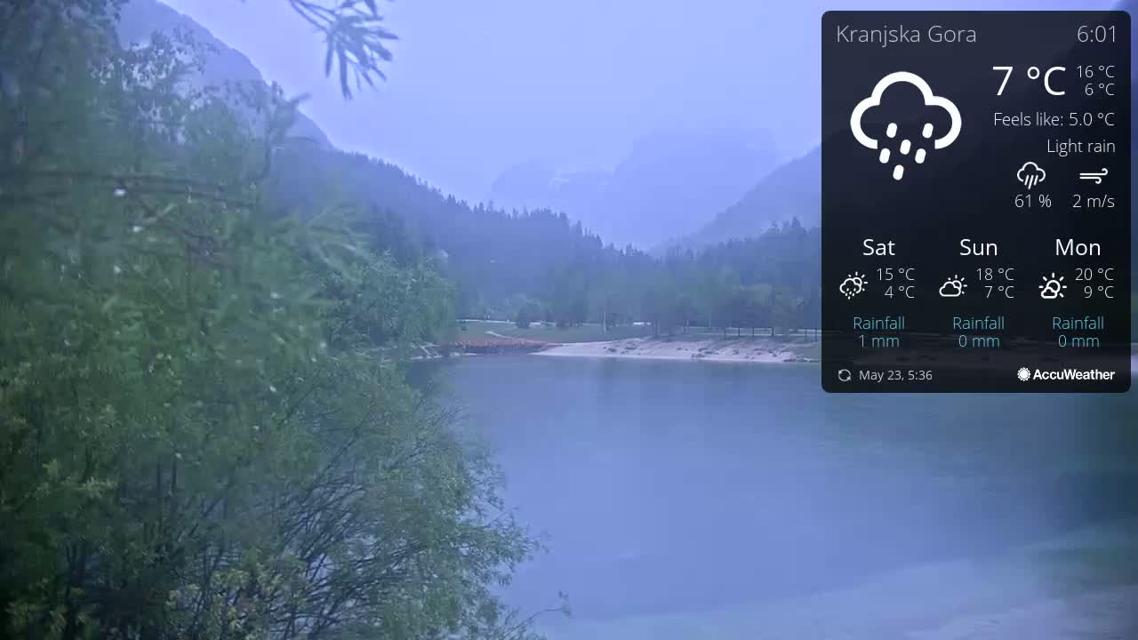 A calm lake is surrounded by misty mountains under a light rain.