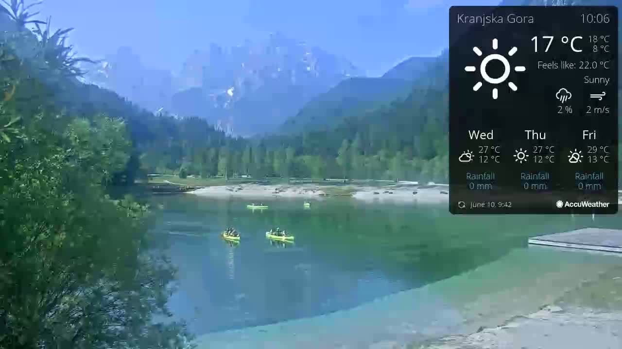 Several canoes are on a calm, turquoise lake surrounded by lush green trees and mountains under a sunny sky.