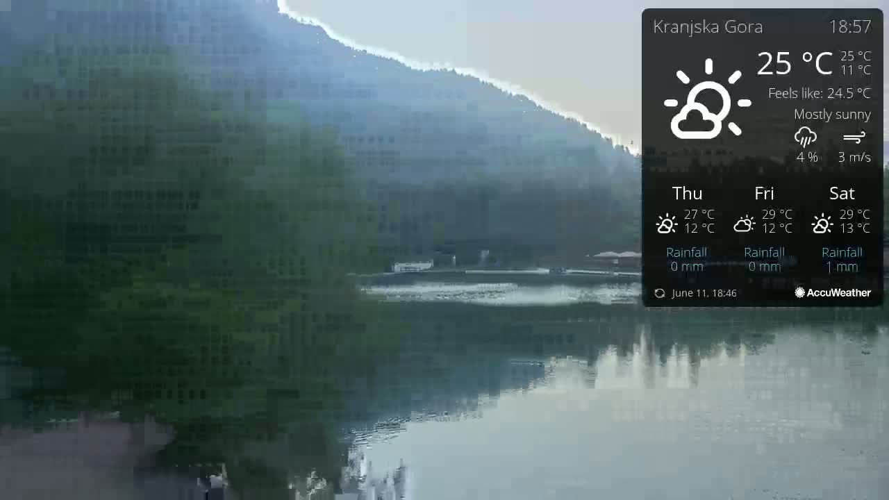 A mostly sunny view of a calm lake reflecting a mountainside under a light haze.