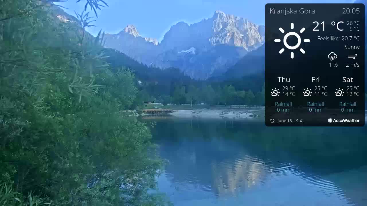 A calm lake reflects mountains under a sunny sky.