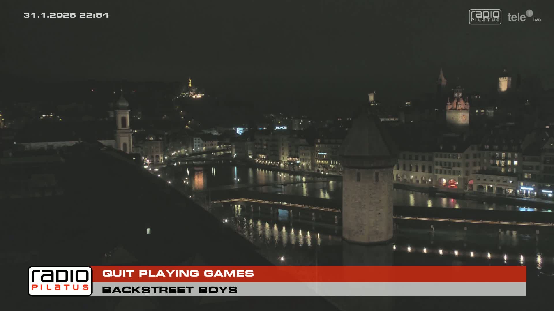 A nighttime, high-angle view of a city with a river running through it, showing buildings illuminated by lights.