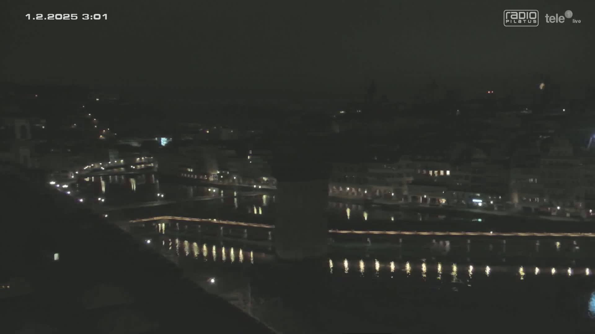 A nighttime, high-angle view of a city with a river reflecting lights, under a clear, dark sky.