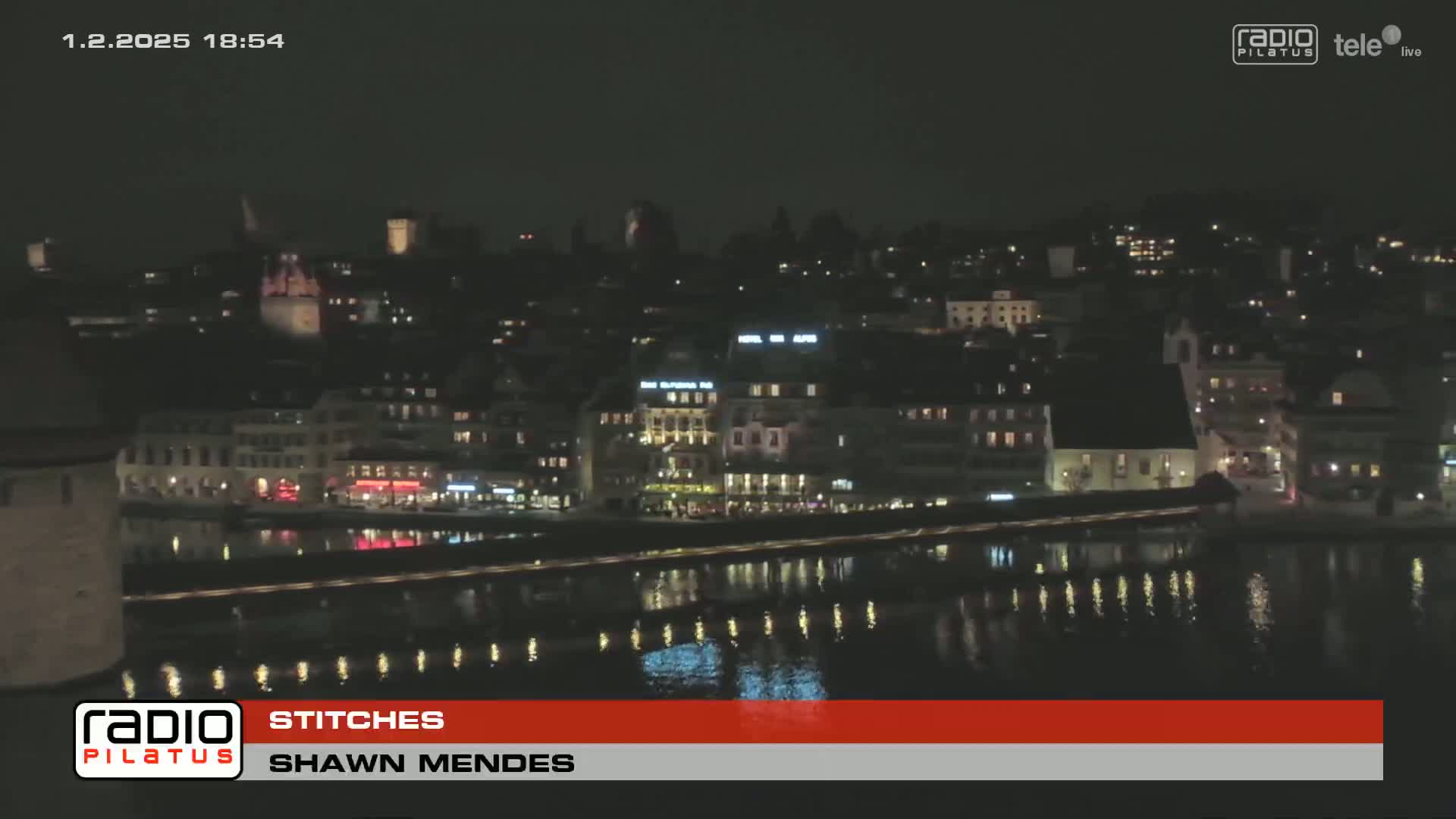 A nighttime view of a city waterfront with illuminated buildings and calm water reflecting the lights.