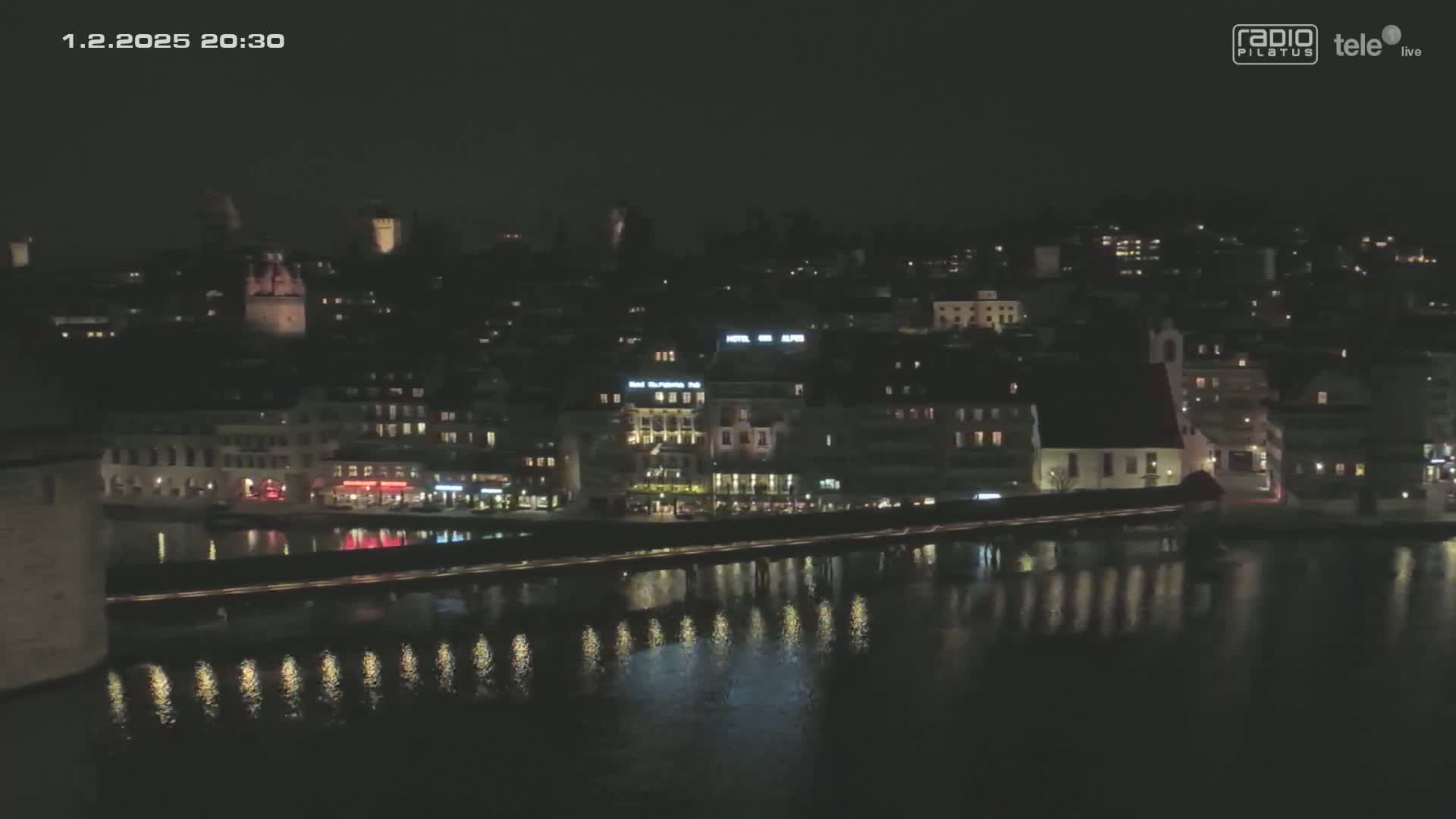 A nighttime view of a city along a body of water, with lights reflecting on the dark water's surface.