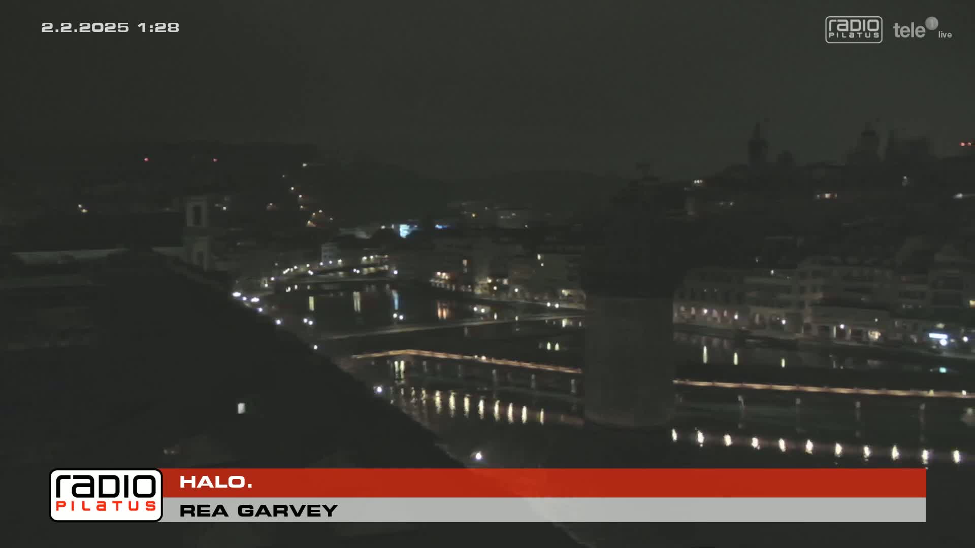 A nighttime view of a city with a river reflecting the lights, under a dark sky.