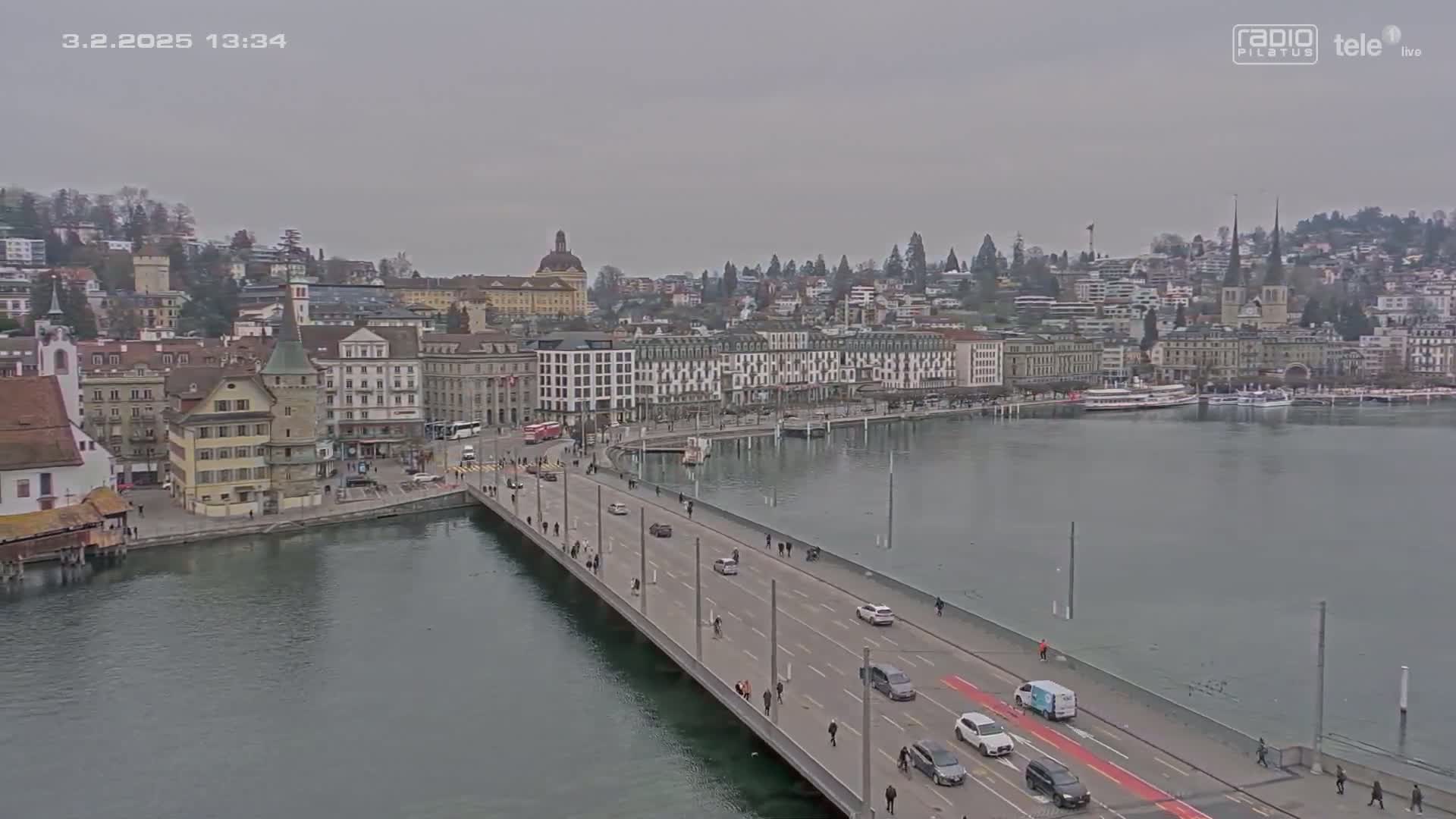 A long bridge stretches across a body of water toward a city with numerous buildings under an overcast sky.