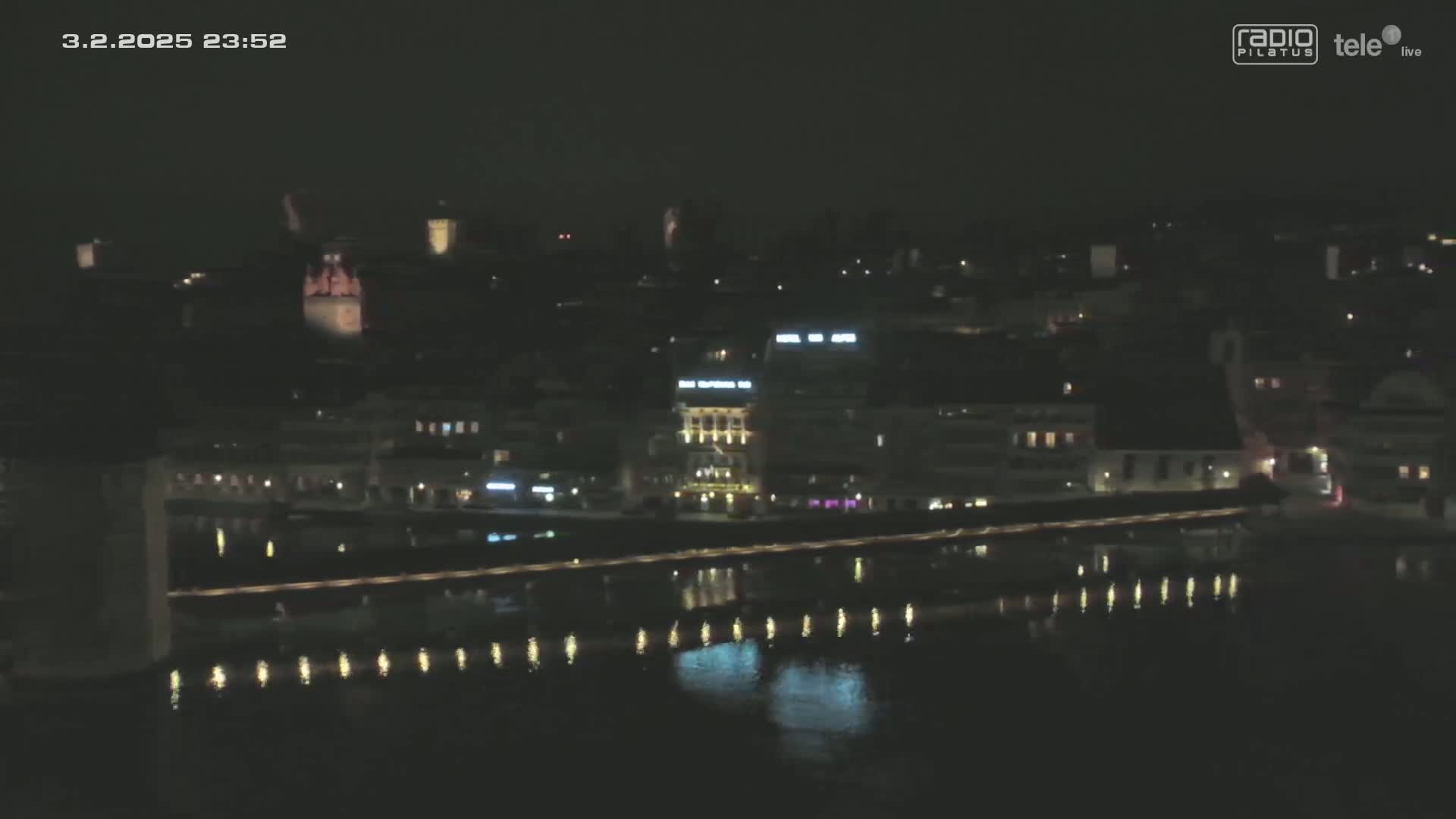 A nighttime view of a city illuminated along a calm river reflecting the lights.