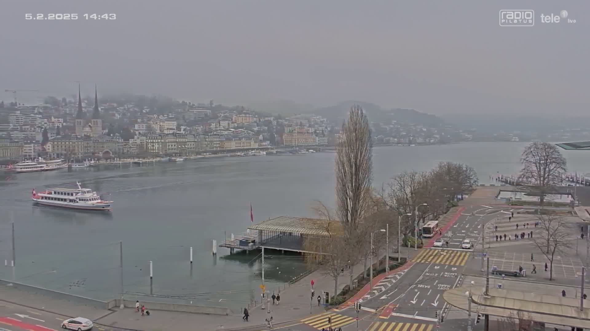A ferry boat is on a lake in front of a city with hazy weather conditions.