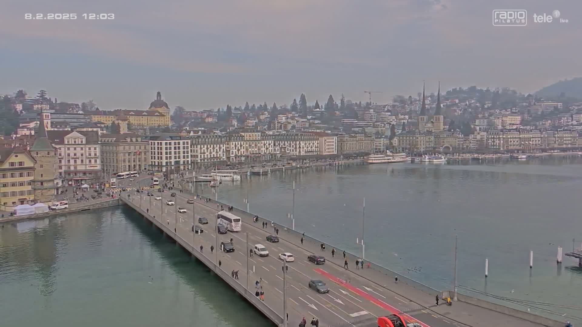 A bridge with light traffic crosses a body of water, leading to a city on a cloudy day.