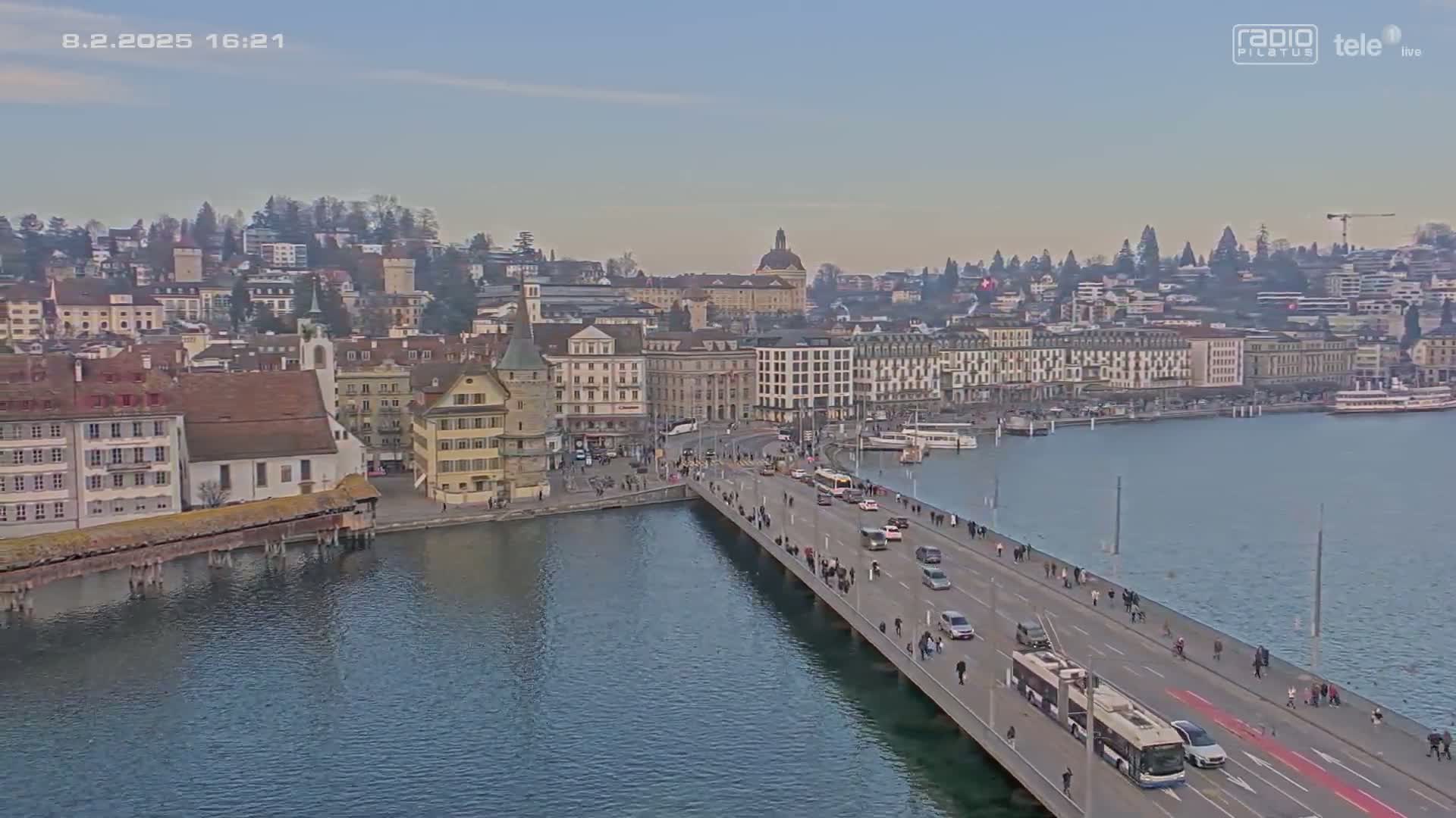 A long bridge extends over calm water toward a city of older buildings under a clear, light-blue sky.
