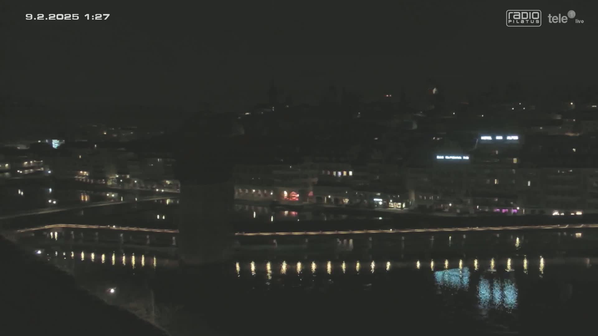 A nighttime view of a city illuminated along a calm body of water.