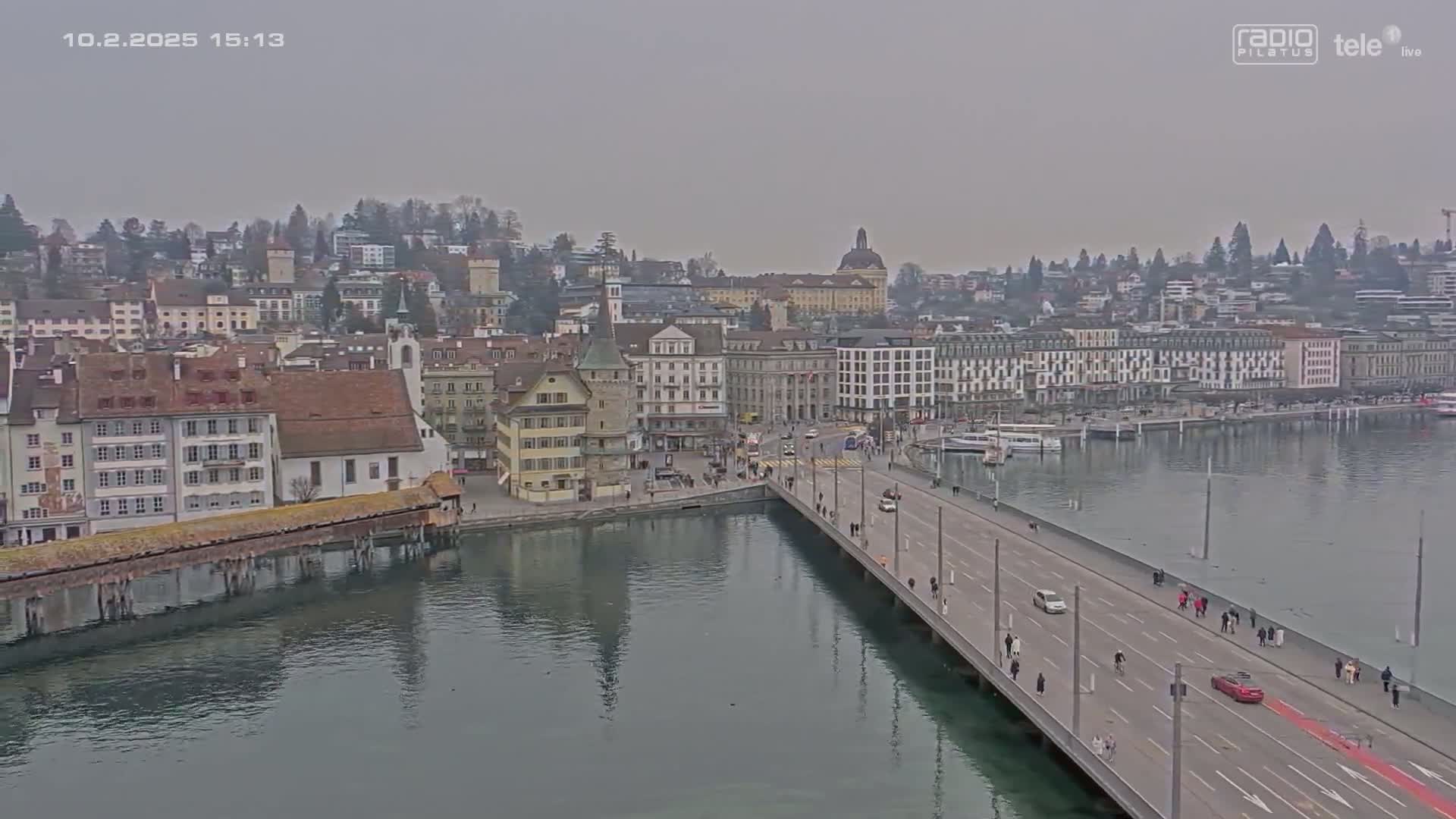 A long bridge extends over calm water toward a city of historic buildings under an overcast sky.